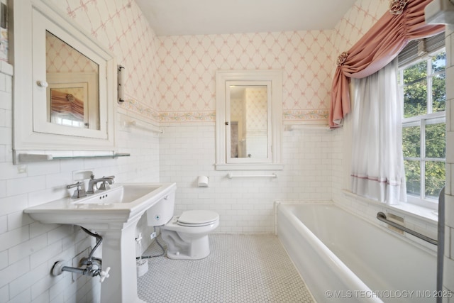 bathroom with wallpapered walls, a garden tub, toilet, and tile walls