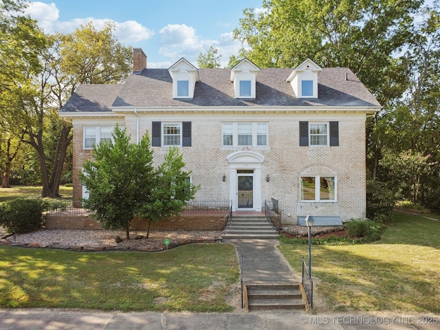 colonial-style house featuring a front yard, brick siding, and a chimney