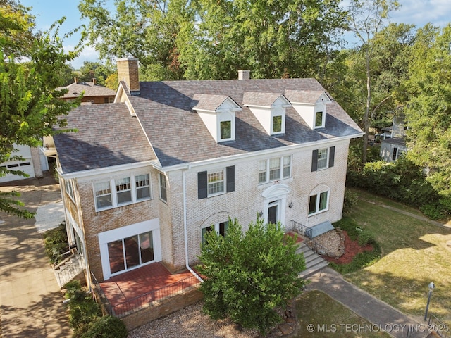 view of front of house with brick siding, a chimney, and a front lawn