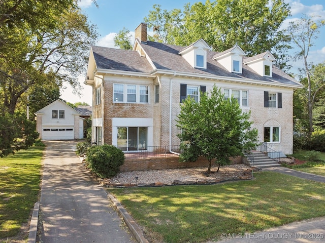 view of front of house featuring a front yard, a chimney, an outdoor structure, a garage, and brick siding