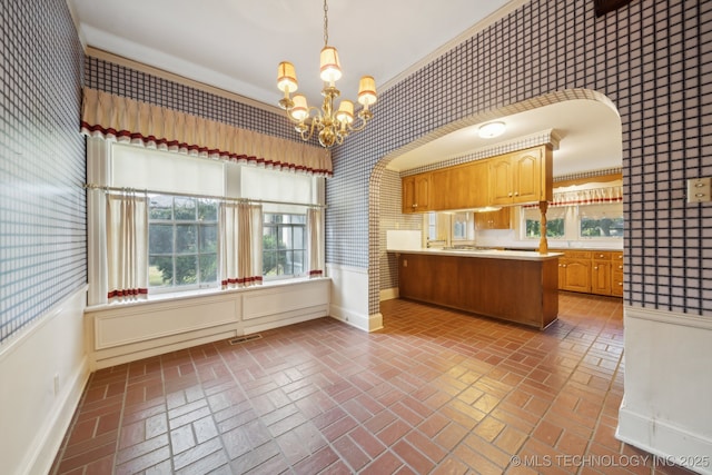 kitchen featuring baseboards, a chandelier, light countertops, a peninsula, and brick floor