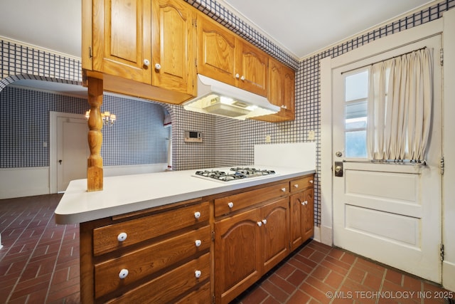 kitchen featuring under cabinet range hood, white gas cooktop, brick floor, and light countertops