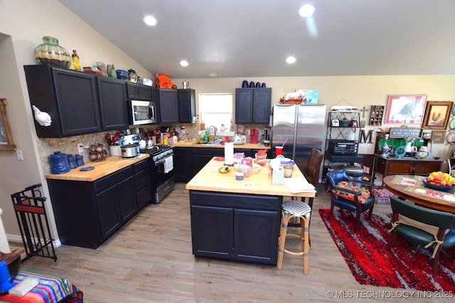 kitchen featuring a sink, a kitchen breakfast bar, tasteful backsplash, stainless steel appliances, and light wood finished floors