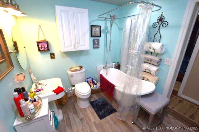 bathroom with curtained shower, a freestanding bath, wood finished floors, and toilet