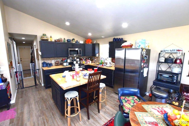 kitchen featuring light wood-style flooring, stainless steel appliances, light countertops, and vaulted ceiling