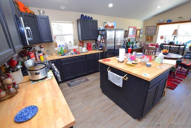 kitchen featuring lofted ceiling, a sink, freestanding refrigerator, light wood finished floors, and wooden counters