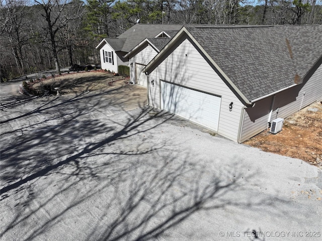 view of side of home featuring an attached garage, driveway, and a shingled roof