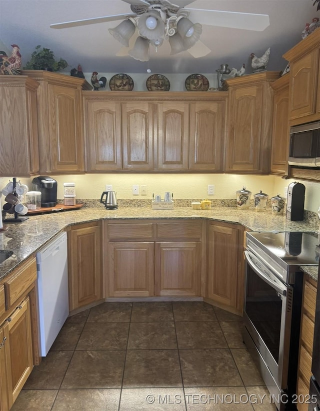 kitchen featuring stainless steel appliances, dark tile patterned flooring, a ceiling fan, and light stone countertops