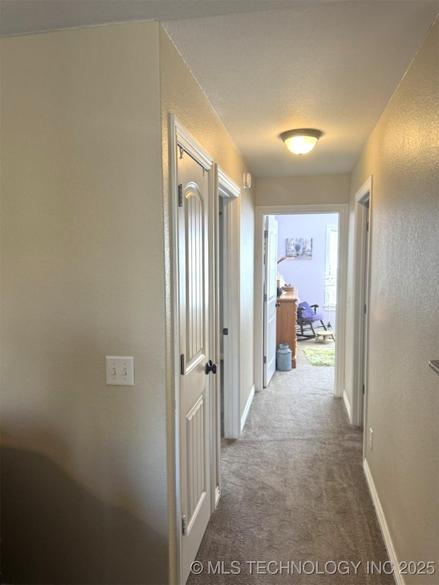 corridor with baseboards, carpet, and a textured wall