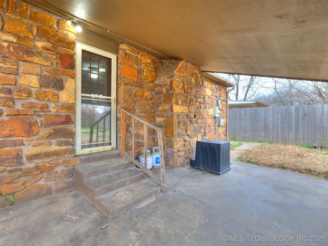 doorway to property with a patio, fence, and stone siding