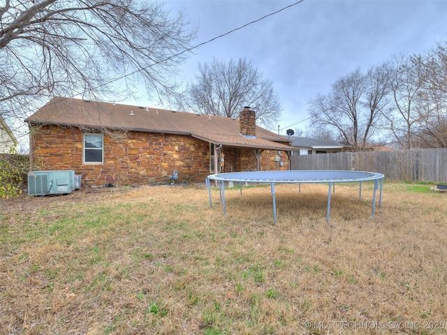 rear view of property featuring stone siding, a trampoline, fence, cooling unit, and a chimney