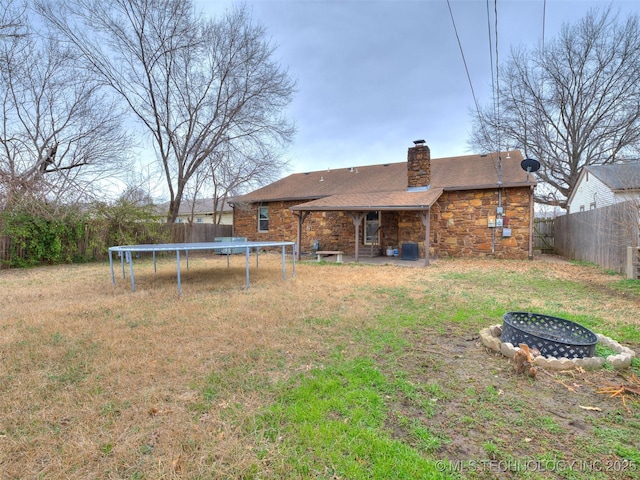 rear view of property featuring a chimney, an outdoor fire pit, a trampoline, and fence