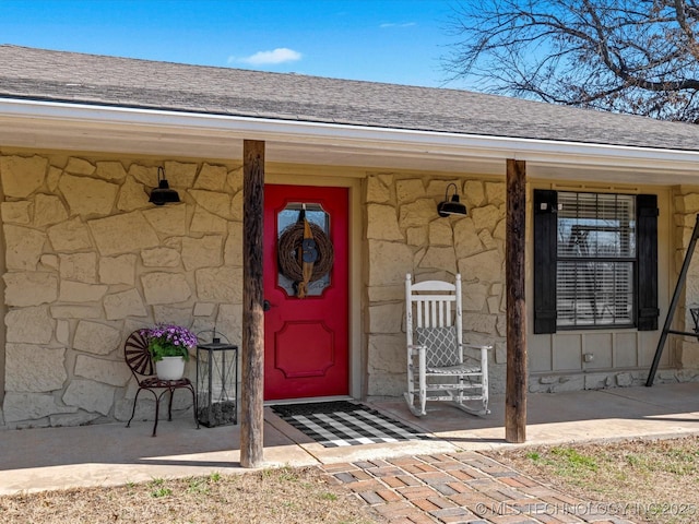 property entrance featuring covered porch, stone siding, and a shingled roof