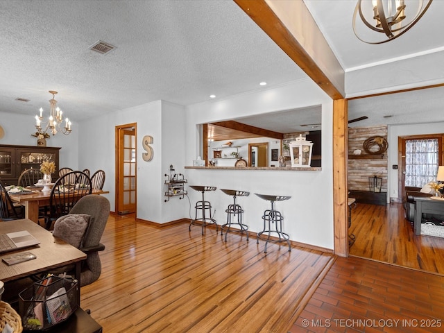 living area with visible vents, a textured ceiling, an inviting chandelier, and wood finished floors