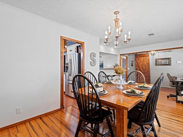 dining area with a barn door, light wood-style floors, and visible vents