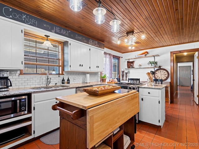 kitchen featuring tasteful backsplash, wooden counters, a kitchen island, white cabinets, and a sink