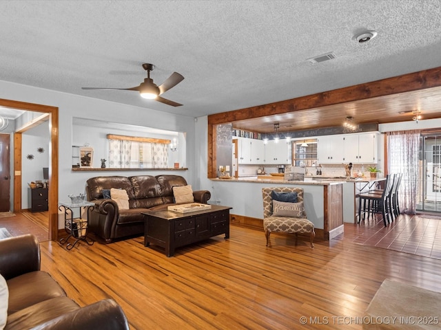 living room featuring ceiling fan, visible vents, a textured ceiling, and wood finished floors