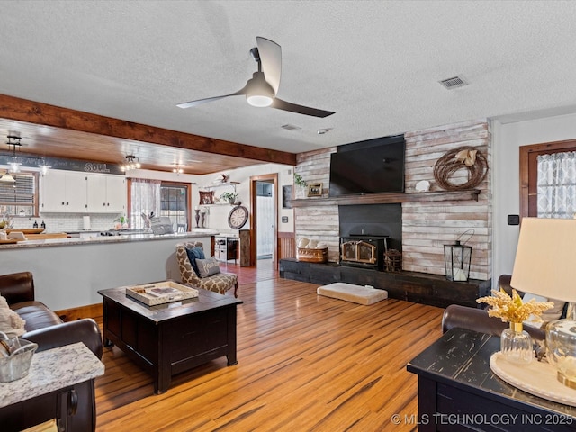 living area with visible vents, a textured ceiling, light wood-style floors, and a ceiling fan