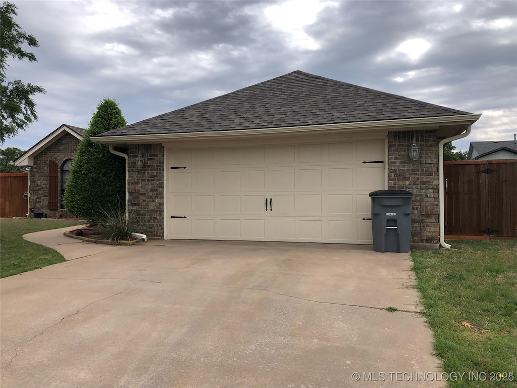 view of side of home with a garage, concrete driveway, roof with shingles, and fence