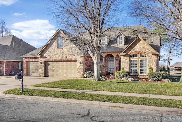 french country inspired facade with an attached garage, a shingled roof, a front yard, stone siding, and driveway