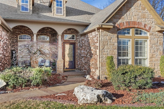 doorway to property featuring stone siding, brick siding, and roof with shingles