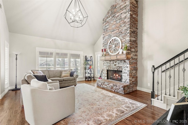 living room with high vaulted ceiling, wood finished floors, an inviting chandelier, a fireplace, and stairs