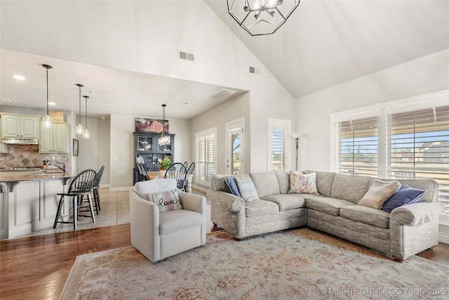 living room featuring an inviting chandelier, high vaulted ceiling, visible vents, and light wood-type flooring