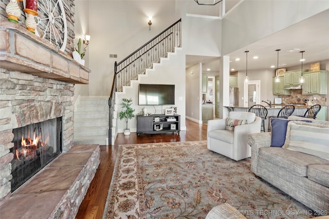 living area featuring dark wood-style flooring, a high ceiling, a fireplace, baseboards, and stairs