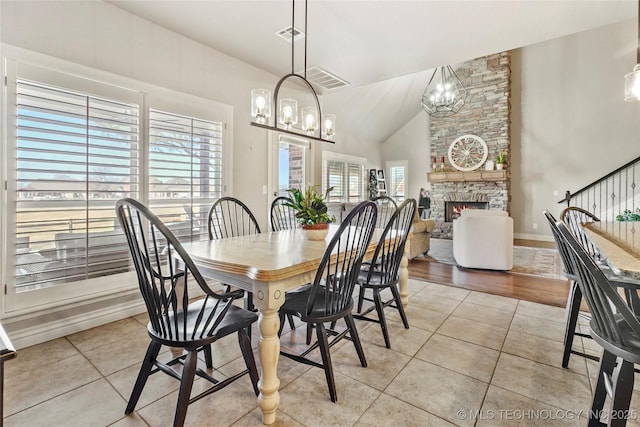 dining room with light tile patterned floors, visible vents, a stone fireplace, and a chandelier