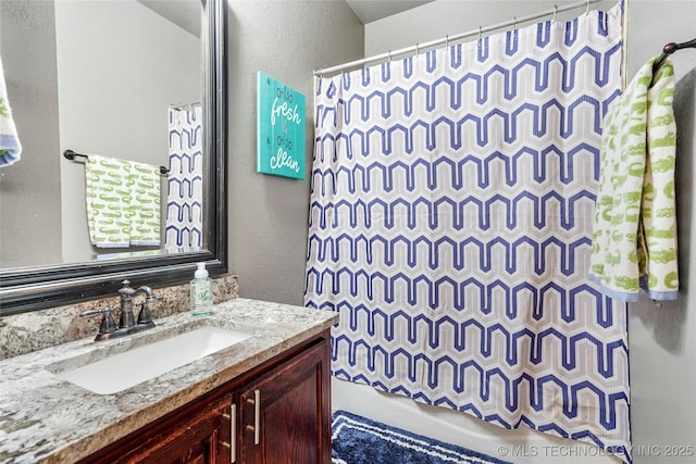 full bath with curtained shower, vanity, and a textured wall