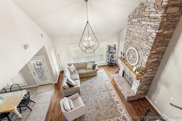 living area featuring visible vents, light wood-style flooring, a stone fireplace, baseboards, and a chandelier