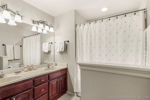 bathroom featuring double vanity, curtained shower, toilet, and a sink