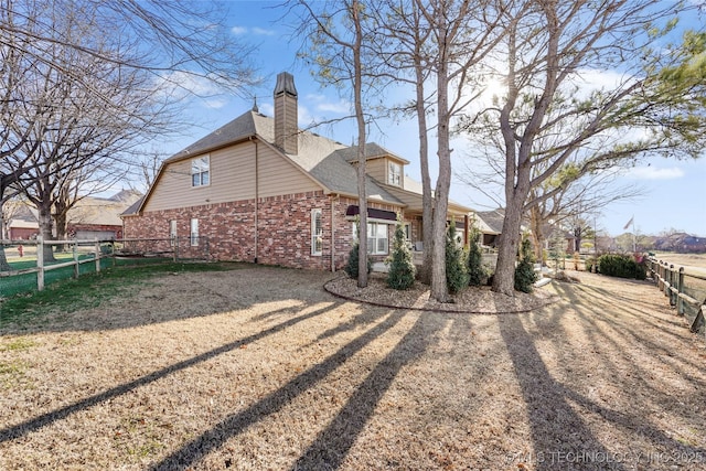 view of side of home with brick siding, a chimney, roof with shingles, and fence