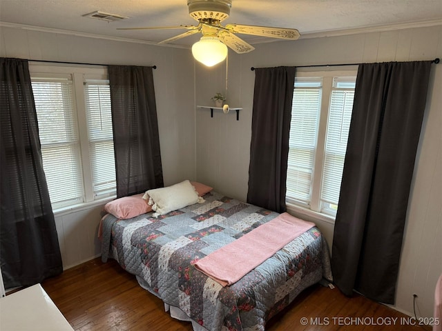 bedroom with a ceiling fan, crown molding, wood finished floors, and visible vents