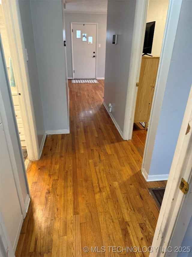 hallway featuring visible vents, baseboards, and hardwood / wood-style flooring