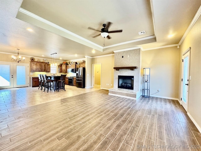 unfurnished living room featuring light wood finished floors, visible vents, a large fireplace, ceiling fan with notable chandelier, and a raised ceiling