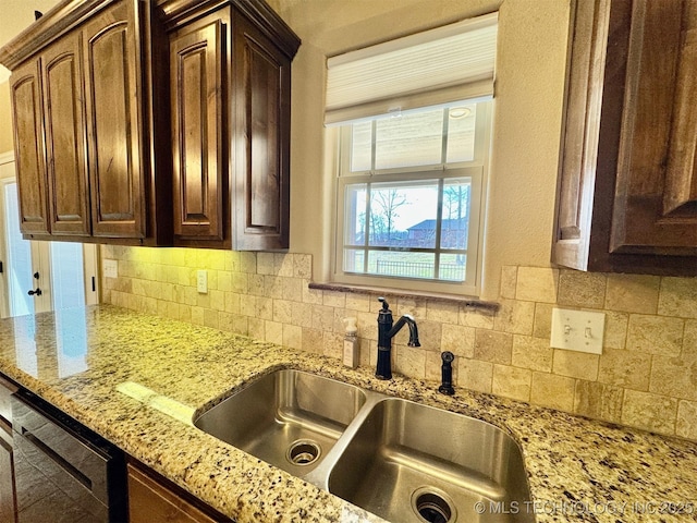 kitchen featuring dark brown cabinets, light stone countertops, tasteful backsplash, and a sink