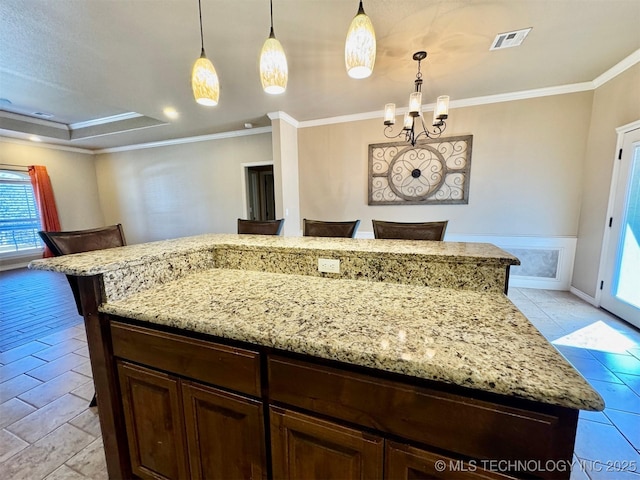 kitchen featuring visible vents, a kitchen island, crown molding, light stone countertops, and decorative light fixtures