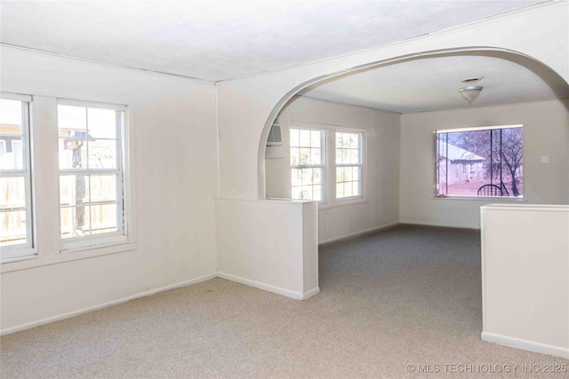 carpeted empty room with arched walkways and baseboards