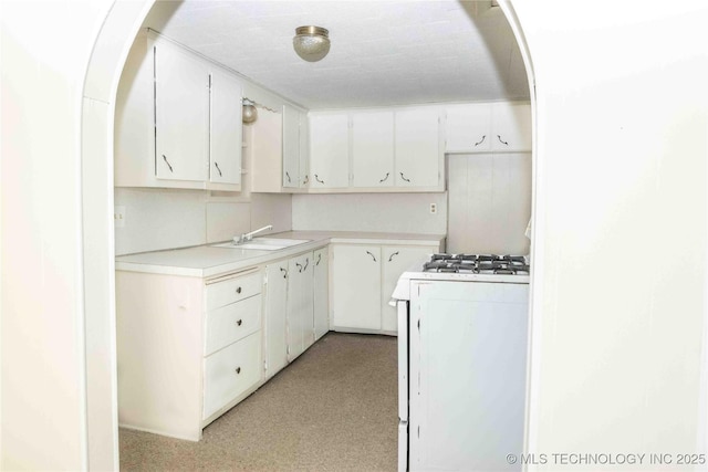kitchen with a sink, white cabinetry, arched walkways, light countertops, and white range with gas stovetop