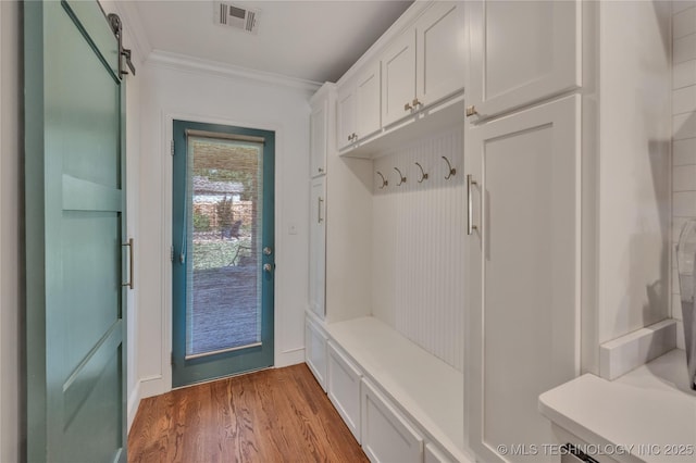 mudroom with a barn door, visible vents, wood finished floors, and ornamental molding