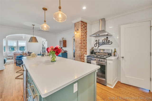 kitchen with green cabinets, gas range, ornamental molding, arched walkways, and wall chimney exhaust hood