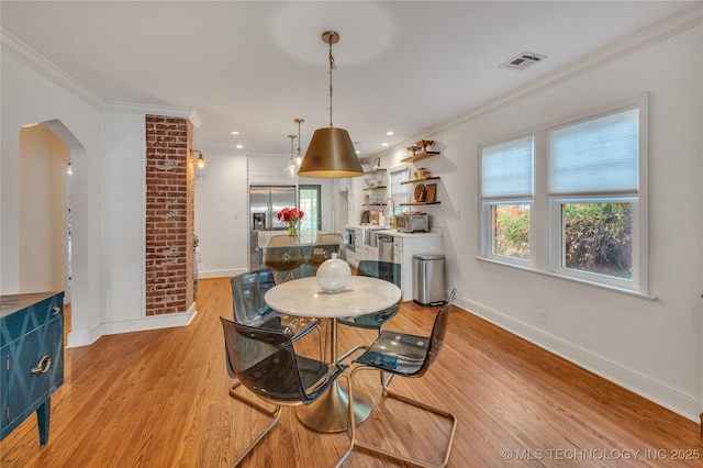 dining area with arched walkways, light wood-style floors, visible vents, and ornamental molding