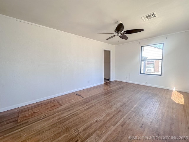 empty room with crown molding, wood finished floors, visible vents, and baseboards