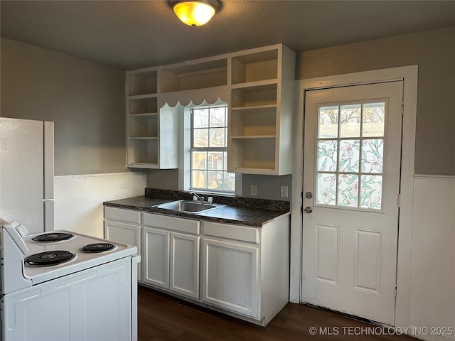 kitchen with open shelves, white appliances, dark countertops, and a sink