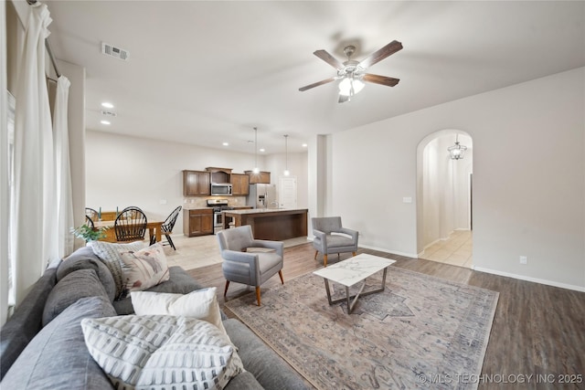 living room featuring visible vents, baseboards, arched walkways, ceiling fan, and light wood-style floors