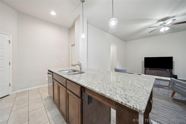 kitchen with light stone countertops, baseboards, an island with sink, arched walkways, and a sink