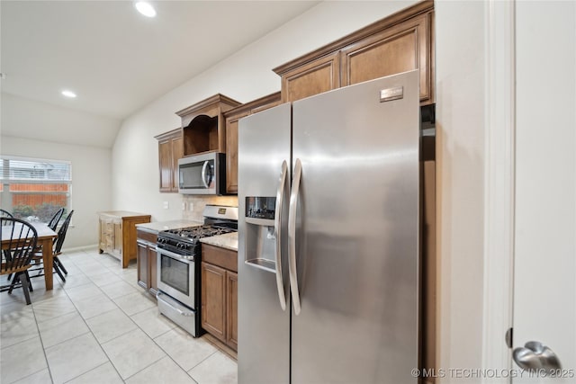 kitchen featuring brown cabinets, recessed lighting, appliances with stainless steel finishes, light tile patterned floors, and vaulted ceiling