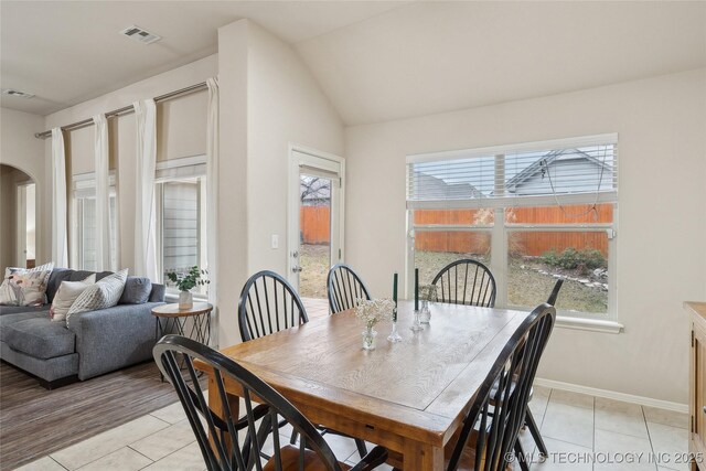 dining room with light tile patterned floors, visible vents, baseboards, arched walkways, and vaulted ceiling