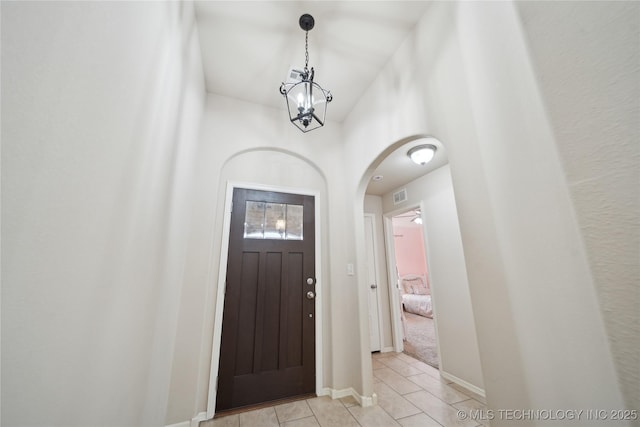 entryway with visible vents, baseboards, light tile patterned flooring, arched walkways, and a chandelier